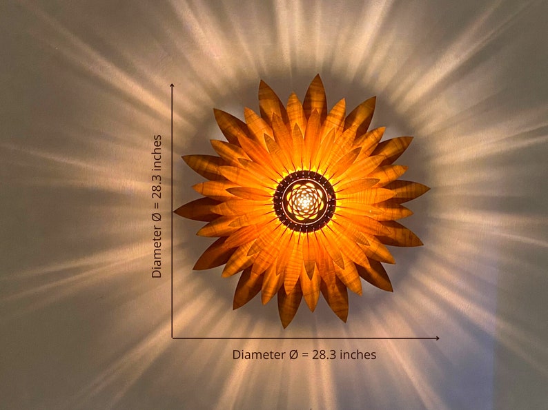 Puede incluir: Una l&aacute;mpara de madera con forma de girasol de 72 cm de di&aacute;metro. La l&aacute;mpara tiene un tono dorado c&aacute;lido y se ilumina desde el centro.