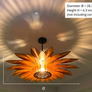 Puede incluir: Una l&aacute;mpara colgante de madera con forma de girasol con un di&aacute;metro de 72 cm y una altura de 16 cm. La luz cuelga del techo y proyecta un brillo c&aacute;lido.