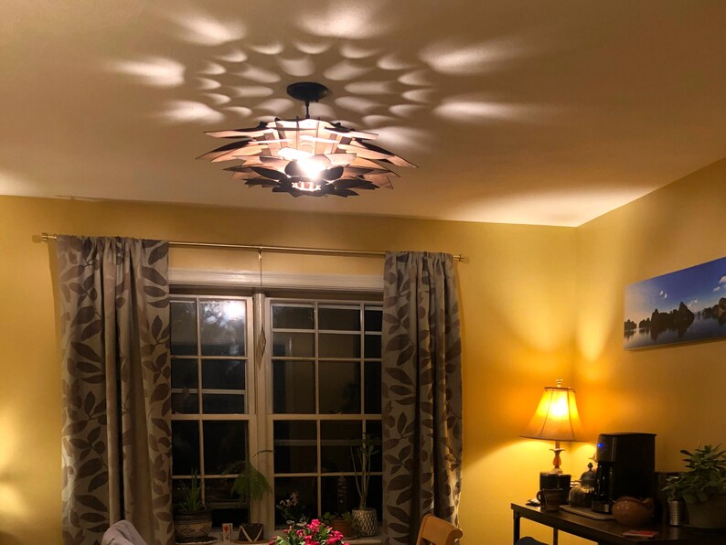 Może przedstawiać: Drewniana lampa sufitowa w kolorze brązowym z unikalnym geometrycznym wzorem rzuca wzorzysty cień na sufit. Lampa jest włączona i oświetla pomieszczenie.