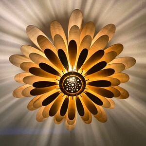 May include: A gold-colored ceiling light fixture shaped like a flower with multiple petals. The light is on and casting a warm glow.