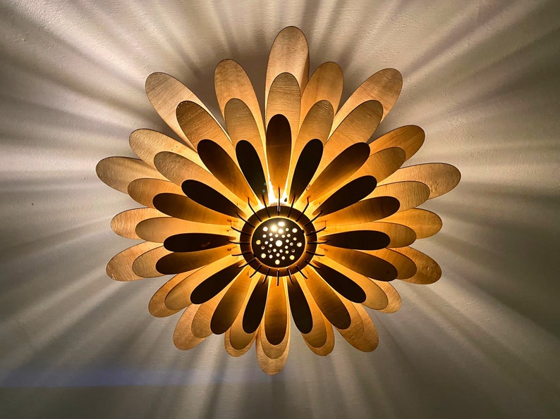 May include: A gold-colored ceiling light fixture shaped like a flower with multiple petals. The light is on and casting a warm glow.