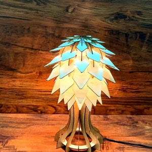 Peut inclure: Lampe de table en bois au design unique. L'abat-jour est compos&eacute; de pi&egrave;ces en forme de losange bleu clair et beige. Le socle est en bois finement d&eacute;coup&eacute;. La lampe est allum&eacute;e, d&eacute;gageant une lueur chaleureuse.