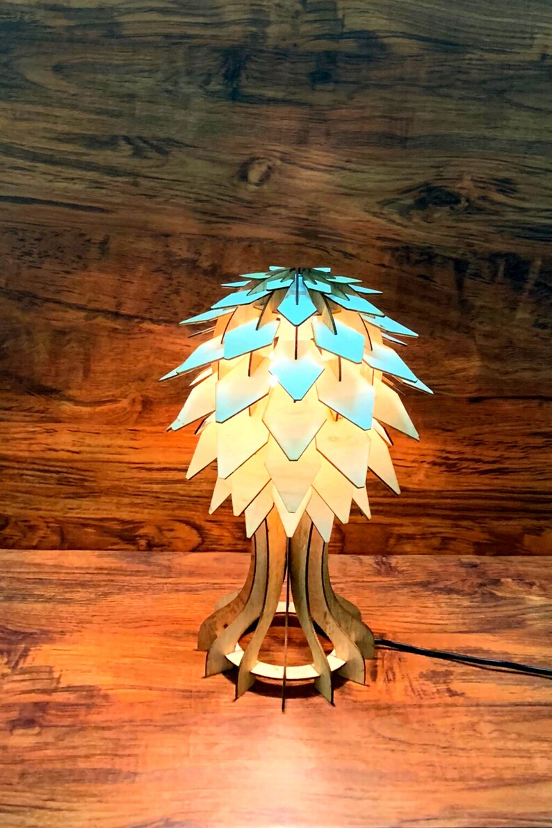Peut inclure: Lampe de table en bois au design unique. L'abat-jour est compos&eacute; de pi&egrave;ces en forme de losange bleu clair et beige. Le socle est en bois finement d&eacute;coup&eacute;. La lampe est allum&eacute;e, d&eacute;gageant une lueur chaleureuse.