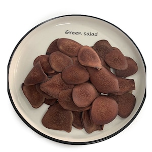 Peut inclure: Une assiette blanche avec une bordure noire, contenant un tas de tranches d'andouiller de cerf séchées et brunes. Le texte "Green salad" est écrit sur l'assiette.