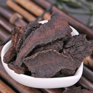 May include: A close-up of a white bowl filled with dried, dark brown, irregularly shaped pieces of root.