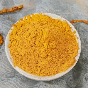 May include: A white bowl filled with a bright yellow powder. The powder is finely ground and has a smooth texture.
