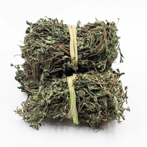 May include: Two bundles of dried green herbs tied together with rubber bands. The herbs are a light green colour and have a slightly brown tint.