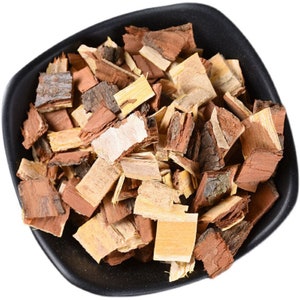 May include: A black bowl containing pieces of tree bark. The bark pieces are various shades of brown, tan, and beige. The bark appears to be cut into small, irregular shapes. The bowl is set against a white background.