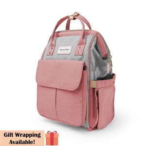 May include: A pink and gray diaper bag backpack with multiple pockets and a zipper closure. The bag has a gold zipper pull and a gold handle. The bag has the text "Sharon Cooper" on the front.