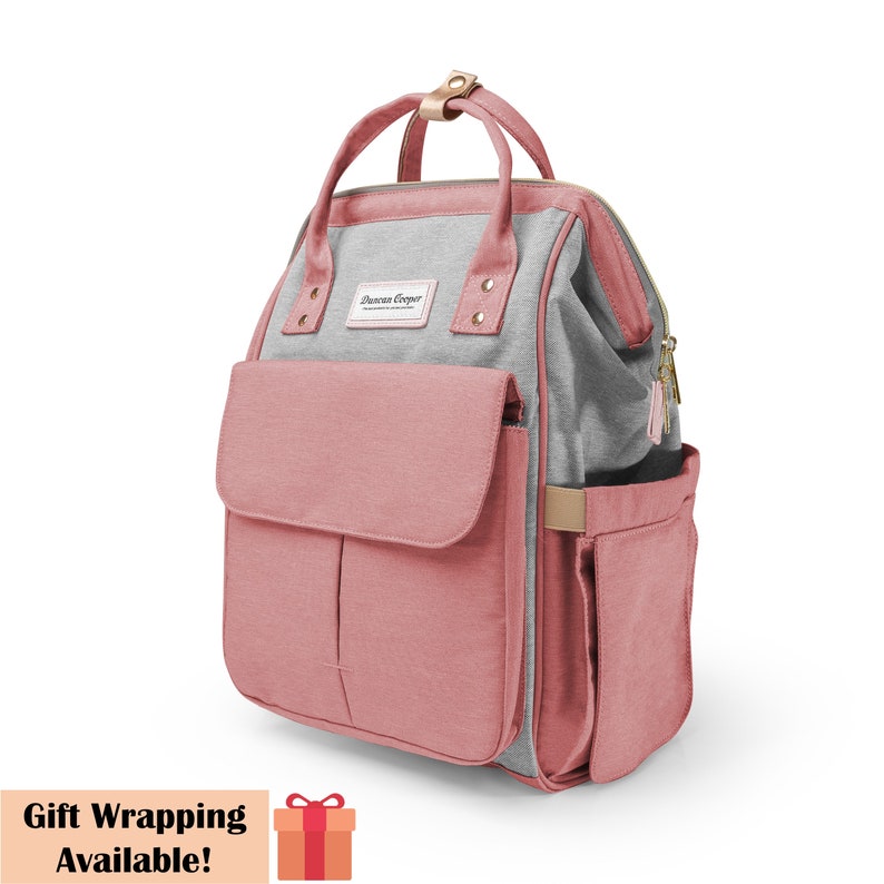 May include: A pink and gray diaper bag backpack with multiple pockets and a zipper closure. The bag has a gold zipper pull and a gold handle. The bag has the text "Sharon Cooper" on the front.