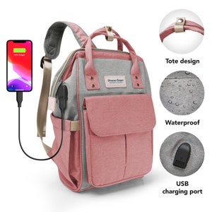 May include: A pink and gray diaper bag backpack with a tote design, a waterproof exterior, and a USB charging port. The bag has a Duncan Cooper logo on the front.