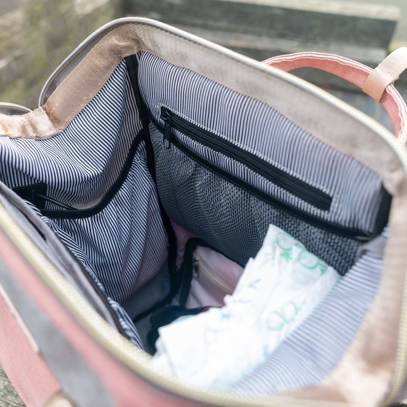 May include: The inside of a pink and beige backpack with a black zippered pocket and a black mesh pocket. The backpack is lined with a black and white striped fabric.