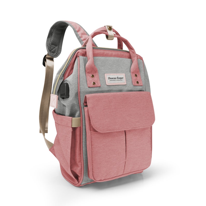 May include: A pink and gray diaper bag backpack with a front pocket and the text "Duncan Cooper" on the front.