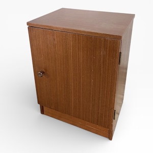 Puede incluir: Un pequeño armario de madera con una sola puerta y un acabado marrón oscuro. El armario tiene un diseño sencillo con un pequeño pomo redondo para abrir la puerta. La veta de la madera es visible en la parte delantera y los laterales.