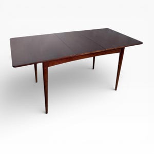 May include: A dark brown, mid-century modern dining table with a rectangular top and four tapered legs. The table has a leaf extension, and is made of wood. The table is shown on a white background.
