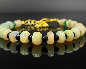 May include: A beaded bracelet featuring opal and dark blue gemstone beads. The opal beads are light yellow with iridescent flashes, and the dark blue beads are faceted. The bracelet has a gold-colored chain and clasp.