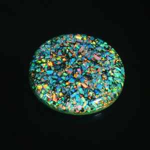 May include: A round, iridescent opal cabochon with a green, blue, and orange color scheme. The opal is made up of many small, shimmering pieces.