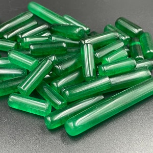 Op de afbeelding: Een stapel groene glazen staven, sommige zijn langer dan andere, allemaal met een gladde, gepolijste afwerking.