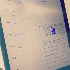 May include: A digital tablet displaying a weekly planner template with handwritten blue ink entries. The layout includes sections for a weekly plan, a to-do list with checkboxes, a habit tracker with blue filled squares, and a notes section with text.
