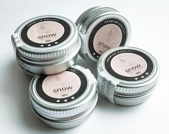 May include: Four small, silver-colored tins of skincare products are arranged on a white surface. Each tin has a black label with the word "snow" and "100%" printed on it. The labels also include the text "Light skin tone" and "Premium Quality".