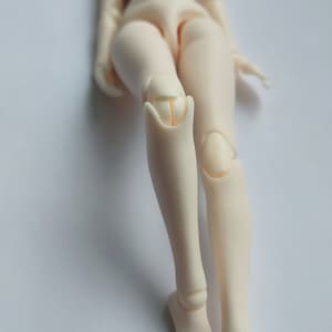 May include: A nude-colored articulated doll with jointed legs and feet. The doll is posed with one leg bent at the knee.