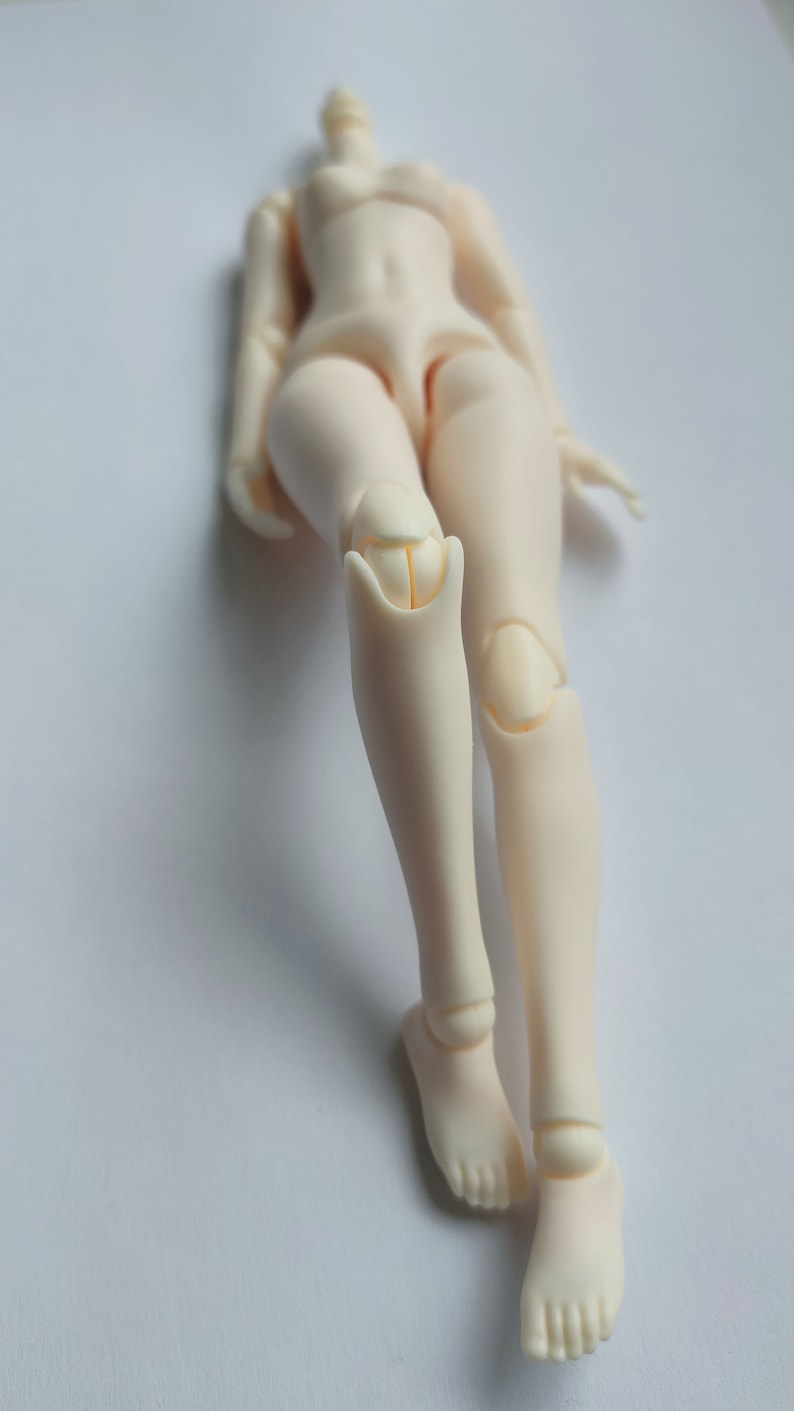 May include: A nude-colored articulated doll with jointed legs and feet. The doll is posed with one leg bent at the knee.