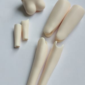 May include: A set of doll body parts, including a torso, two upper legs, two lower legs, and two arms. The parts are made of a smooth, off-white plastic.