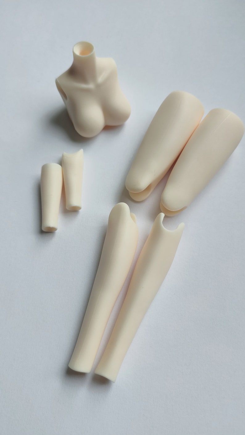 May include: A set of doll body parts, including a torso, two upper legs, two lower legs, and two arms. The parts are made of a smooth, off-white plastic.