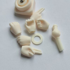 May include: A set of doll parts including hands, arms, and a head. The parts are made of a smooth, off-white plastic.