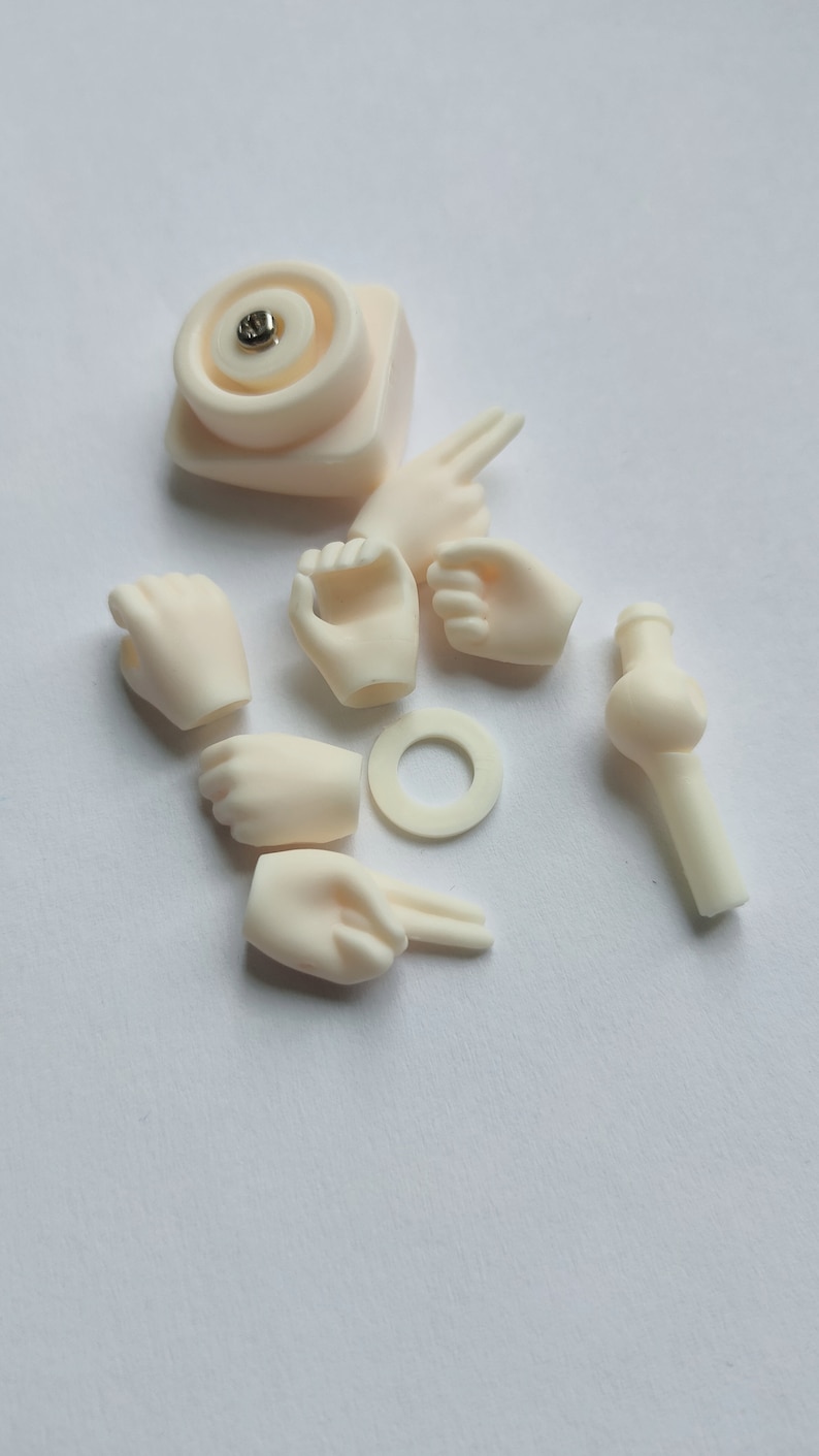 May include: A set of doll parts including hands, arms, and a head. The parts are made of a smooth, off-white plastic.