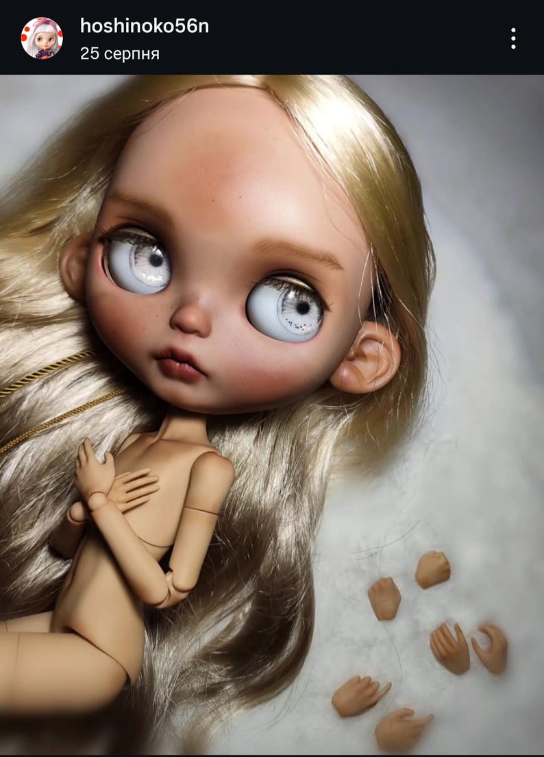 May include: A ball-jointed doll with long, straight blonde hair, large pale blue eyes, and a tan complexion. The doll has articulated limbs and is positioned with hands near the chest. Five additional interchangeable hand pieces are included.