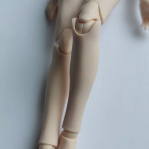 May include: A close-up of a doll's legs, showing the articulated knee joints. The legs are made of a smooth, light-colored plastic.
