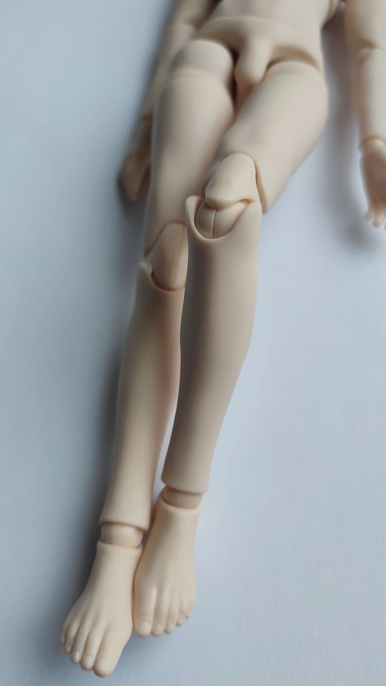 May include: A close-up of a doll's legs, showing the articulated knee joints. The legs are made of a smooth, light-colored plastic.