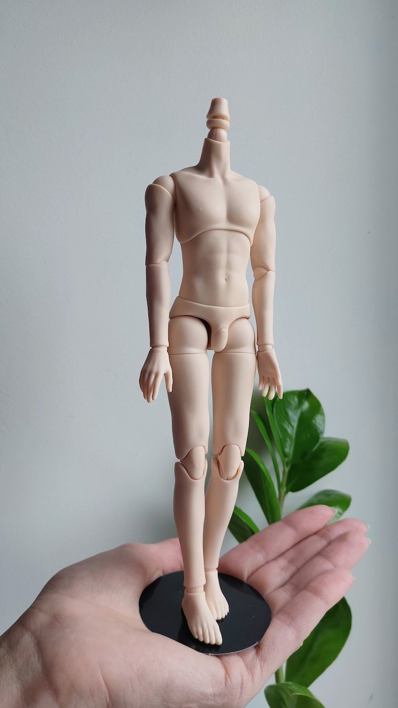 May include: A nude-colored articulated doll body with a jointed neck, arms, legs, and feet. The doll is standing on a black circular base.