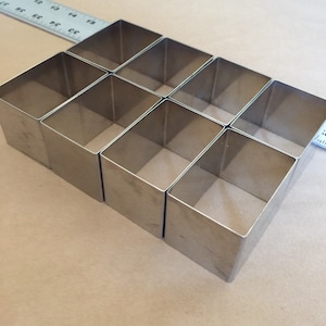 以下が含まれることがあります： 茶色の表面に、銀色の金属製の正方形のケーキリングが9つ、交互に配置されています