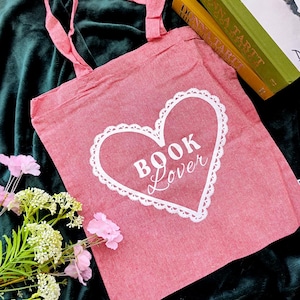Op de afbeelding: Roze canvas draagtas met witte handvatten en een wit hartontwerp met de tekst "Book Lover".