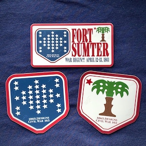 Könnte beinhalten: Drei Aufkleber mit einem rot-weißen Rand. Ein rechteckiger Aufkleber lautet "FORT SUMTER WAR BEGUN!!! APRIL 12-13, 1861" mit einer Palmen-Grafik. Die anderen beiden Aufkleber haben einen blauen Hintergrund mit weißen Sternen und dem Text "1863.DESIGNS CIVIL WAR 165".