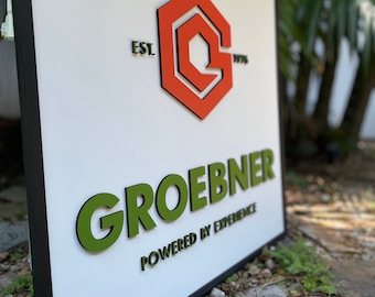 May include: A white sign with a black frame, featuring a red and white logo with the text "EST. 1976". The sign also has the text "GROEBNER POWERED BY EXPERIENCE" in green raised letters.
