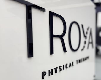 May include: A white sign with black lettering that reads "TROYA PHYSICAL THERAPY".