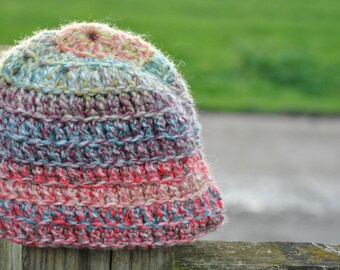 May include: A colorful crocheted hat with a variety of shades of blue, pink, and beige. The hat is made with a textured stitch and has a slouchy fit.