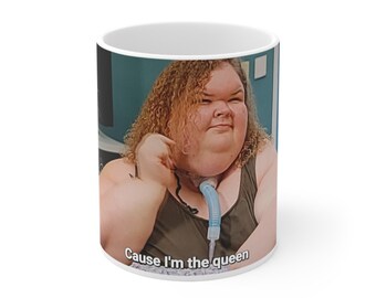 Peut inclure: Une tasse en céramique blanche avec une photo d'une femme aux cheveux bouclés et un tube médical bleu autour du cou. Le texte "Cause I'm the queen" est imprimé au bas de la tasse.