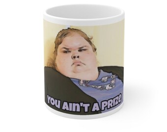 Peut inclure: Une tasse à café en céramique blanche avec une image de dessin animé d'une femme avec une expression sérieuse. Le texte "You ain't a prize" est imprimé sur la tasse.