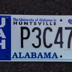 May include: White license plate with blue text and a blue and white logo that says "UAH" and "The University of Alabama in HUNTSVILLE". The license plate number is "P3C47" and the state is "ALABAMA". There is a small blue sticker that says "HEART OF DIXIE" in the top right corner.