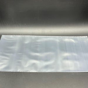 May include: A clear plastic bag, flat and smooth, with a slight sheen. The bag is empty and appears to be made of a thin, flexible material.
