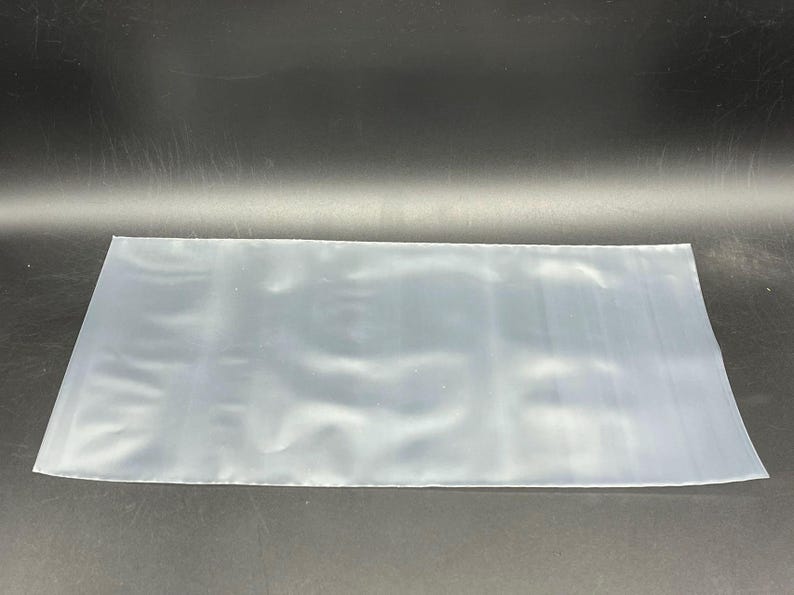 May include: A clear plastic bag, flat and smooth, with a slight sheen. The bag is empty and appears to be made of a thin, flexible material.