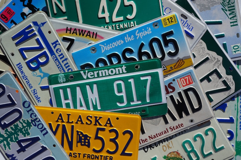 May include: A collection of license plates from different states, including Vermont, Alaska, Oregon, Kentucky, and Hawaii. The plates are arranged in a random order and feature various colors, including green, blue, yellow, and white. The plates display different license plate numbers, state names, and slogans.