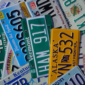 May include: A collection of vintage license plates from different states, including Hawaii, Vermont, Kentucky, Alaska, Oregon, and others. The plates are in various colors, including blue, green, yellow, and white. Some of the plates have text on them, such as "Discover the Spirit" and "The Natural State".
