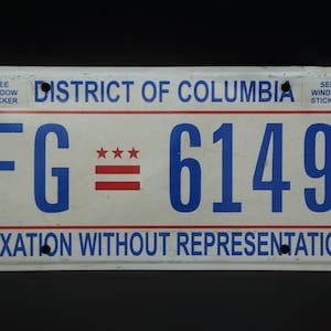 May include: A white District of Columbia license plate with blue text reading FG 6149 and TAXATION WITHOUT REPRESENTATION. The plate features three red stars and two red horizontal bars in the center, with SEE WINDOW STICKER in the top corners.