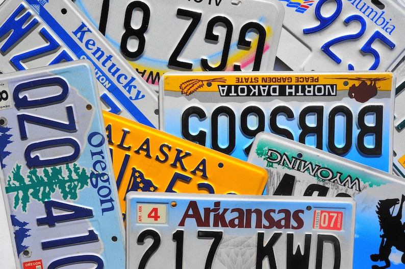 May include: A close-up of various license plates from different states in the United States. The plates are arranged in a random pattern and feature different colors, fonts, and designs. The plates include the states of Kentucky, Oregon, North Dakota, Alaska, Wyoming, and Arkansas.