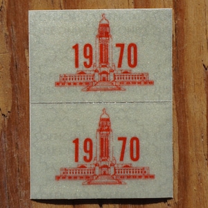 May include: Two vintage silver stickers with a red building illustration and the year 1970 printed in red.